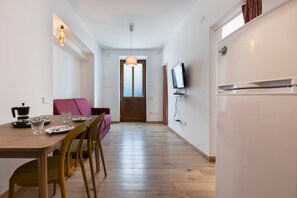 A modern kitchen with a dining area, wooden flooring, and a television mounted on the wall.