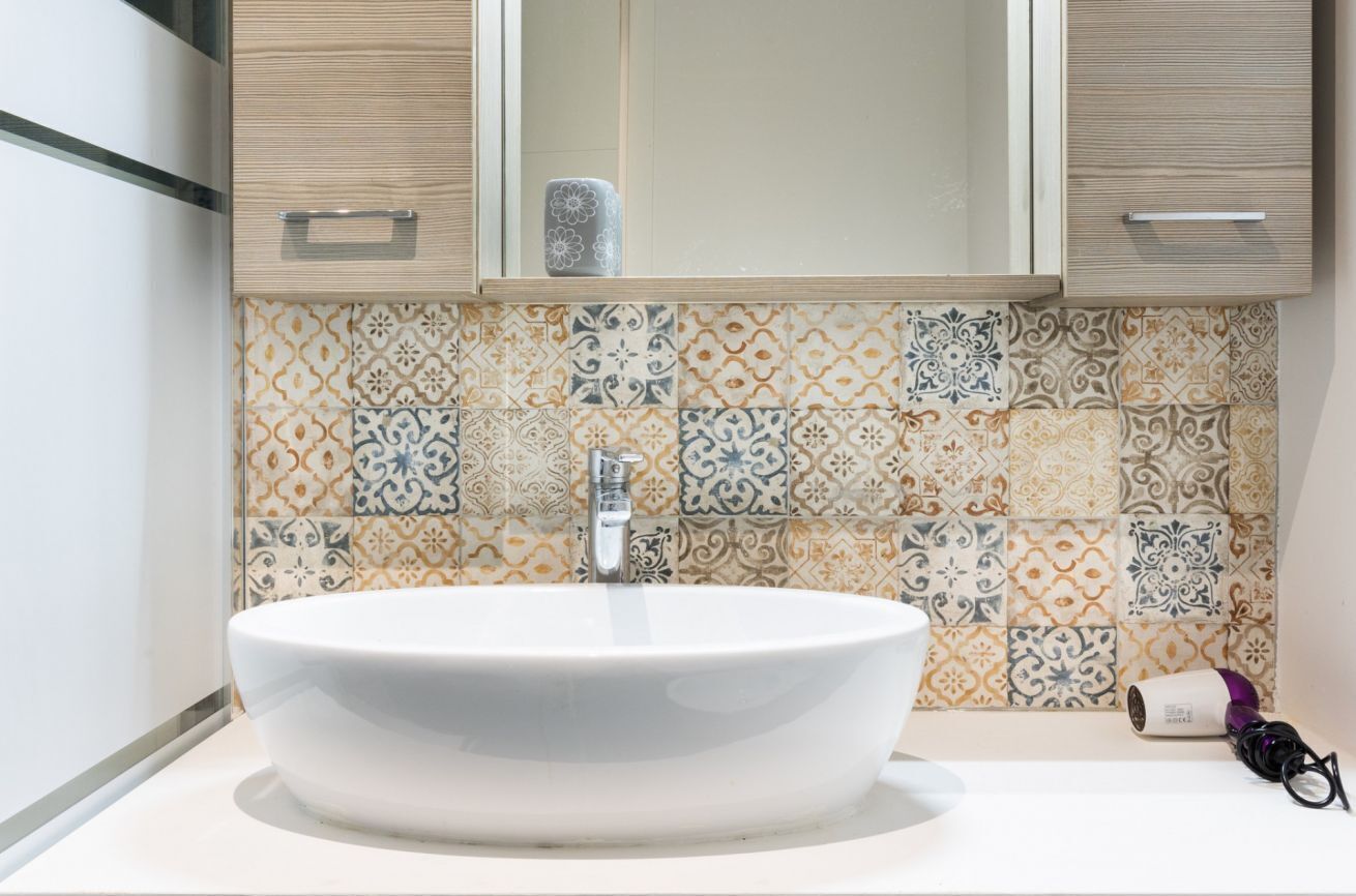 A bathroom with a white sink, patterned tiles, and wooden cabinets.