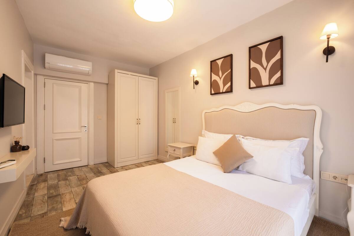 A bedroom with a bed, bedside tables, a TV, wardrobe, and wall-mounted lights.