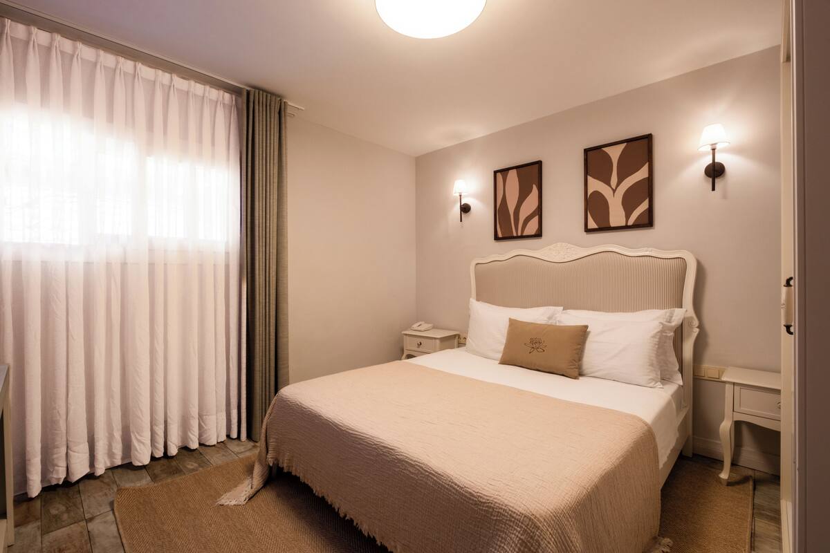A bedroom with a large bed, a nightstand, a lamp, and a window with curtains.