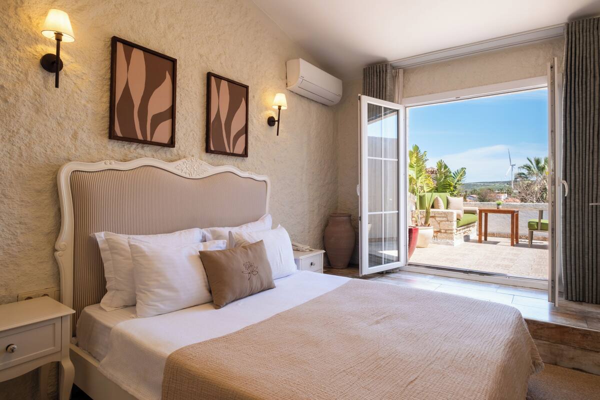 A bedroom with a bed, bedside tables, wall-mounted lamps, and a large window with a view of the outdoors.