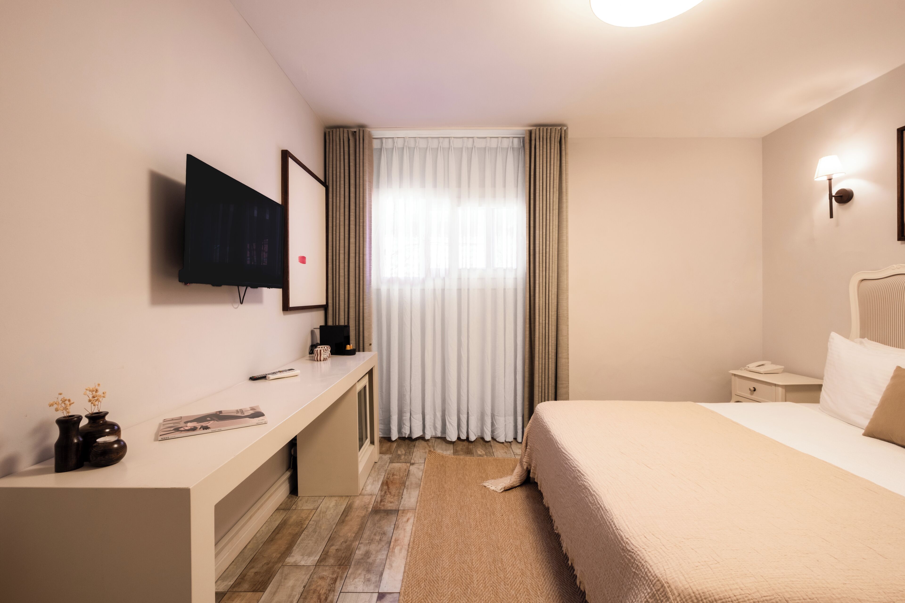 Une chambre d’hôtel avec un lit, un bureau, une télévision et une fenêtre avec des rideaux.