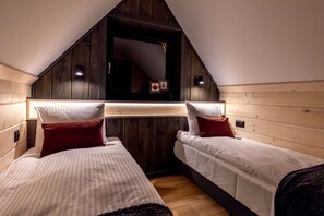 Quarto com duas camas, painéis de madeira e teto inclinado.