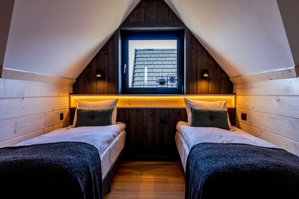 A cozy attic bedroom with two beds, wooden walls, a skylight, and a small window.