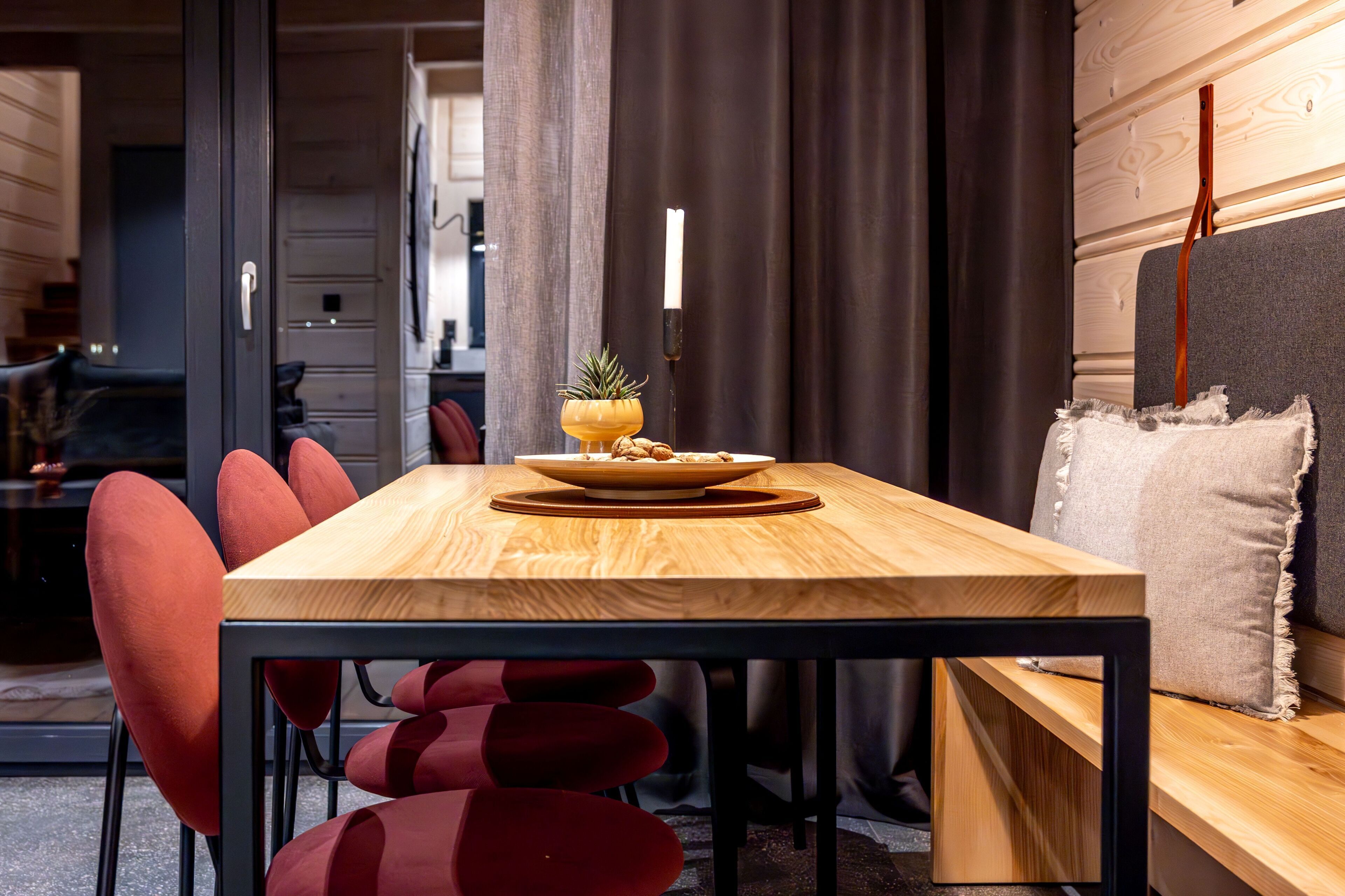 A modern dining area with a wooden table, red chairs, and a candle centerpiece.