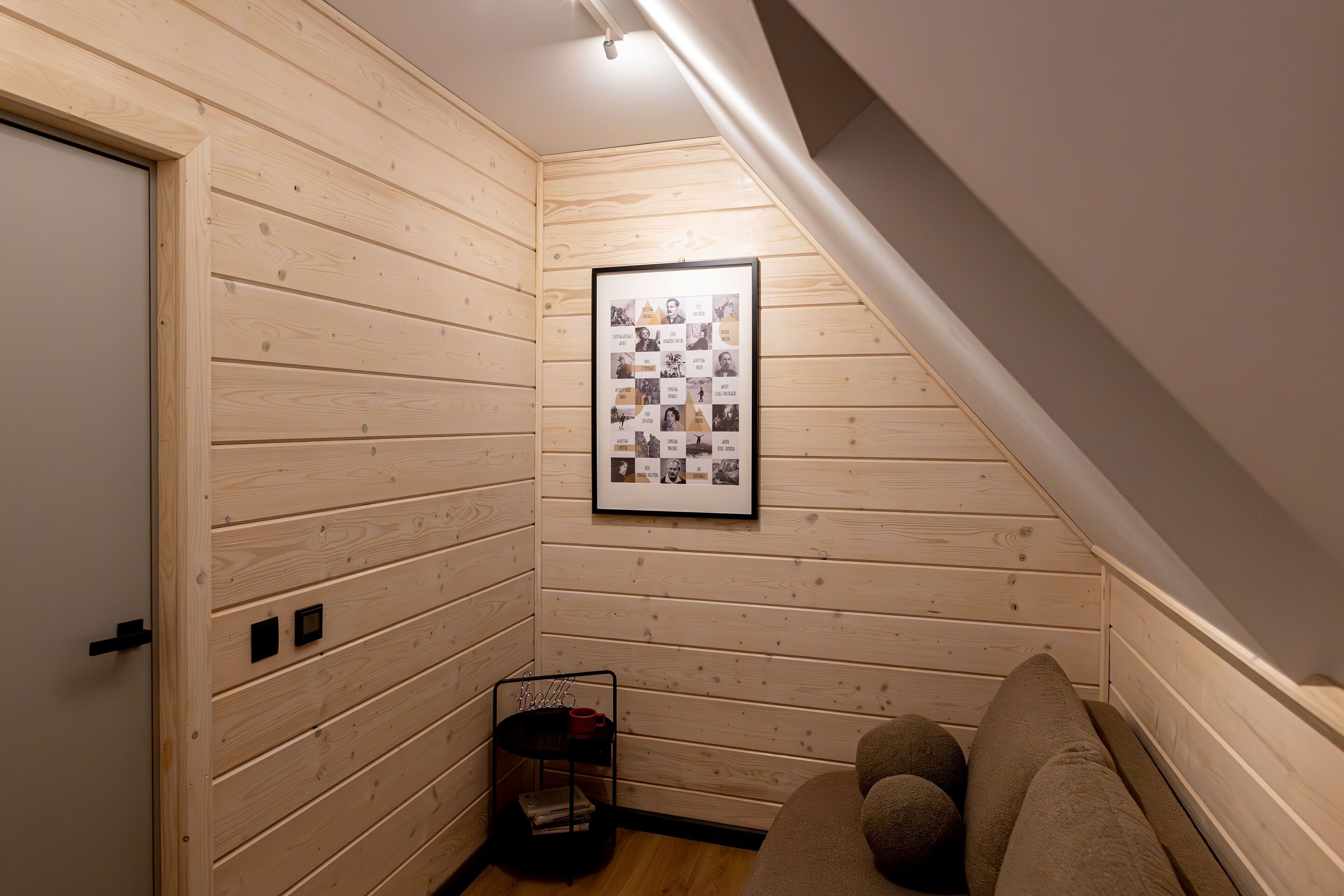 A cozy room with wooden walls, a framed collage on the wall, a small shelf with items, and a sofa.