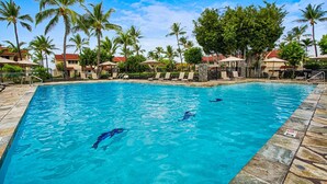 A swimming pool with clear blue water, surrounded by palm trees and lounge chairs.