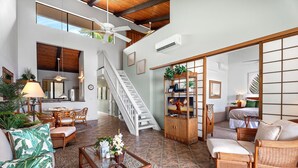 A spacious living area with a high ceiling, a staircase, wicker furniture, and a television.