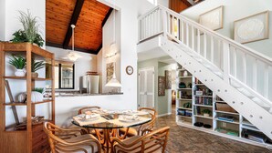 A dining area with a round glass table, wooden chairs, a bookshelf, and a staircase.