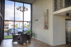 A spacious lobby with large windows, a chandelier, a dining area with wicker furniture, and a view of the parking lot and buildings outside. - 138 El Matador 2 Bedroom Condo (Fort Walton Beach)