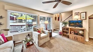 Una sala de estar acogedora con un ventilador de techo, un televisor y una ventana con vistas a una terraza.