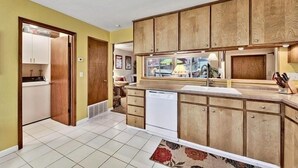 Una cocina con armarios de madera, lavavajillas y ventana con vista a la calle.