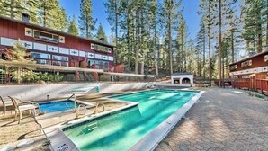 Un área de piscina con una piscina azul cristalina, un pequeño pabellón y un edificio de fachada roja y ventanas blancas.
