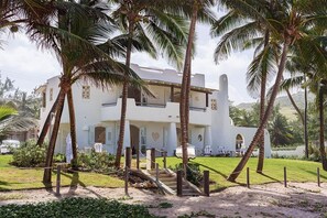 A white building with a staircase, surrounded by palm trees and a well-maintained lawn. - Pebble 3 Bedroom Home (Bathsheba)