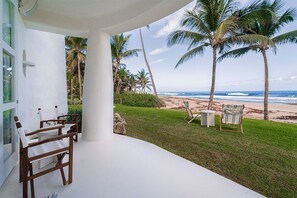 A covered outdoor seating area with a view of the beach and palm trees. - Pebble 3 Bedroom Home (Bathsheba)