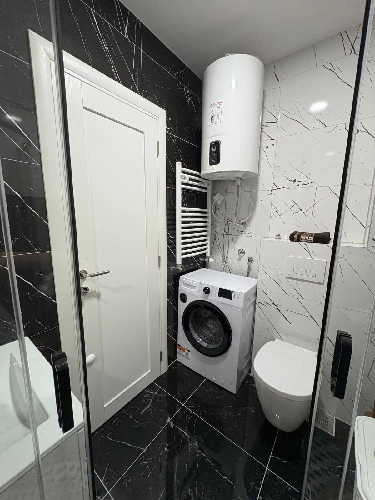 A compact bathroom with a washing machine, toilet, and a water heater.