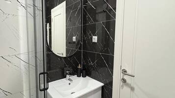 Un bany amb un lavabo blanc, un mirall i parets de marbre negre.