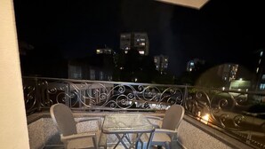 A balcony with a table and two chairs, a metal railing, and a cityscape view at night. - I&I Apartments 36 (Kragujevac)