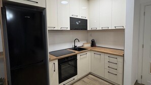 A compact kitchen with white cabinets, a black refrigerator, a built-in oven, and a microwave. - I&I Apartments 36 (Kragujevac)