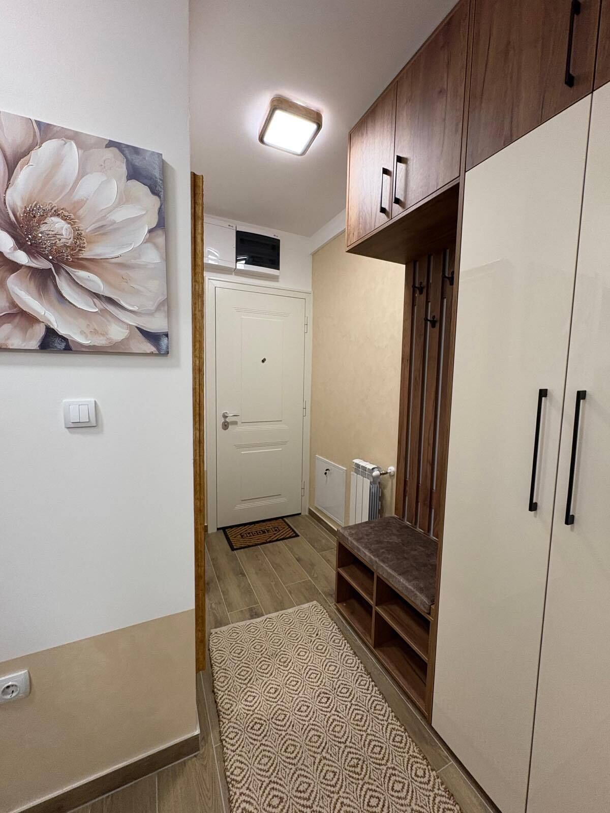 A hallway with a wooden wardrobe, a white door, and a floral painting on the wall.