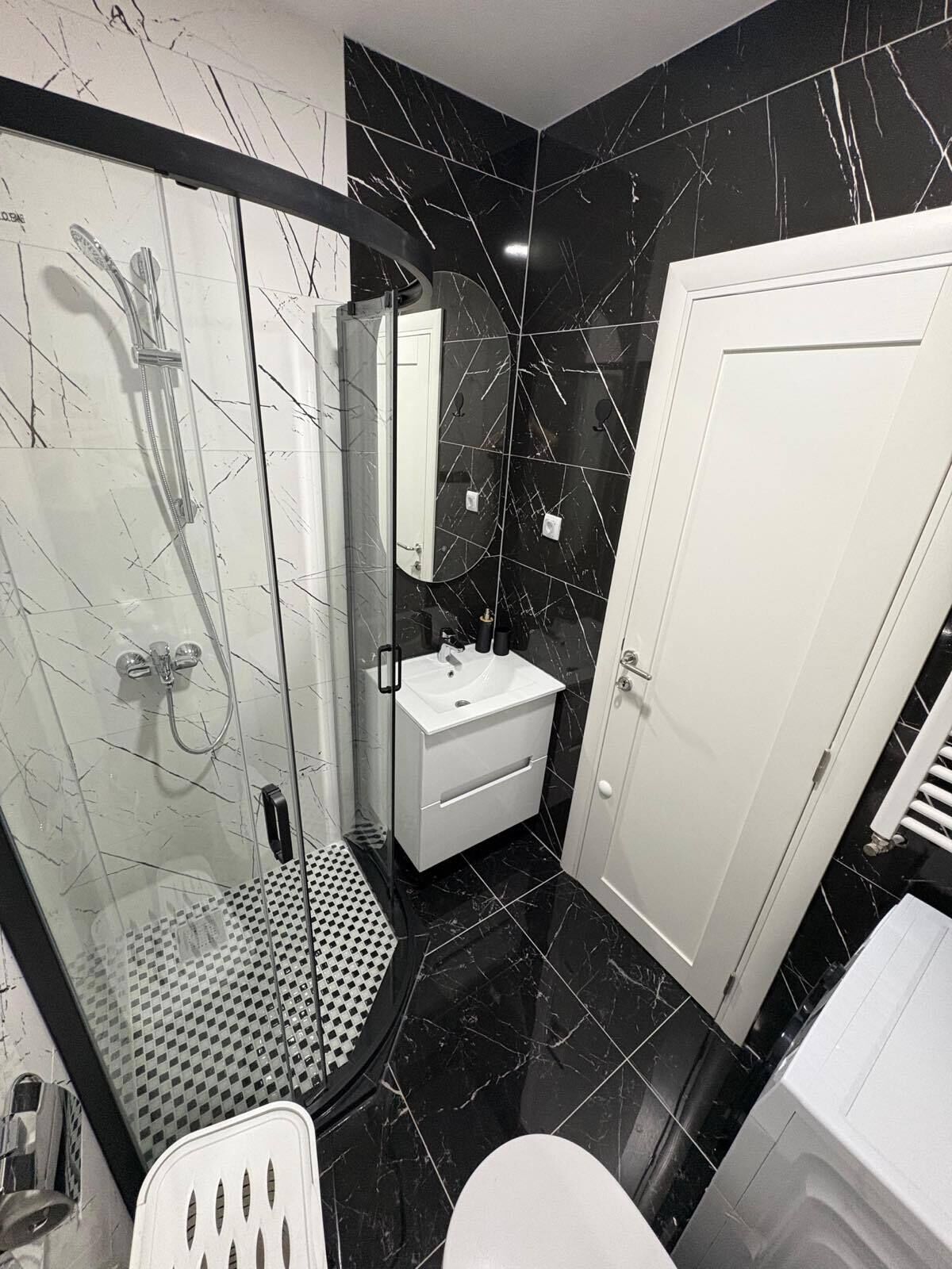 Une salle de bain moderne avec une douche à parois de verre, un lavabo blanc et une porte blanche.