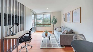 Un salon moderne comprenant un canapé, une table basse, un bureau avec une chaise et une grande fenêtre donnant sur la ville.