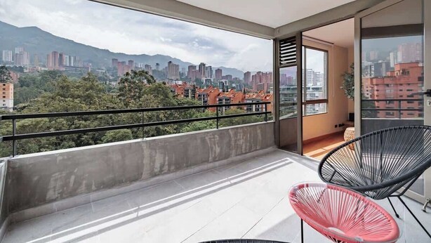 Un balcon avec vue sur la ville, deux chaises et un sol en béton.
