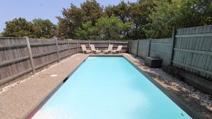A rectangular swimming pool with a tiled edge, surrounded by a wooden fence and a gravel area. - Sunny Cape Cod Poolside Haven (2407) (Truro)