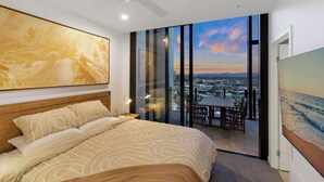 Un dormitorio con cama, ventilador de techo, mesita de noche, ventana grande y balcón con mesa y sillas.