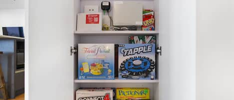 A shelf with various board games including Trivia Pursuit, Tapple, Connect 4, and Pictionary.