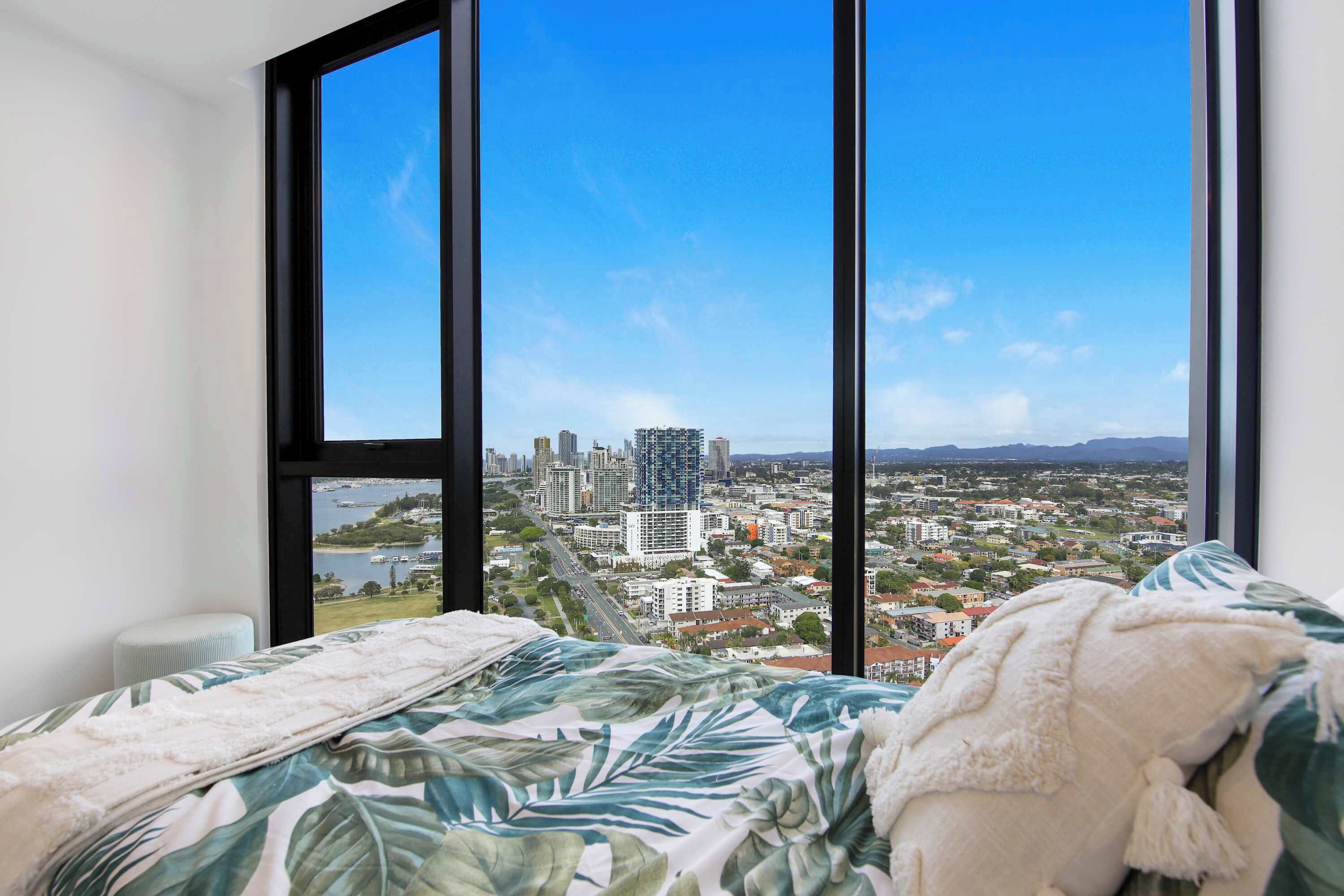 A bedroom with a large window, a bed with a floral bedspread, and a view of a cityscape.