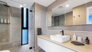 Un baño moderno con ducha envuelta en vidrio, un lavabo blanco y un espejo grande.