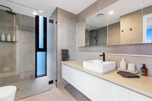 A modern bathroom with a glass-enclosed shower, a white sink, and a large mirror.