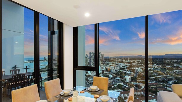 Un comedor con mesa lista para cuatro personas, ventanas amplias con vista a la ciudad y un balcón con mesa y sillas.