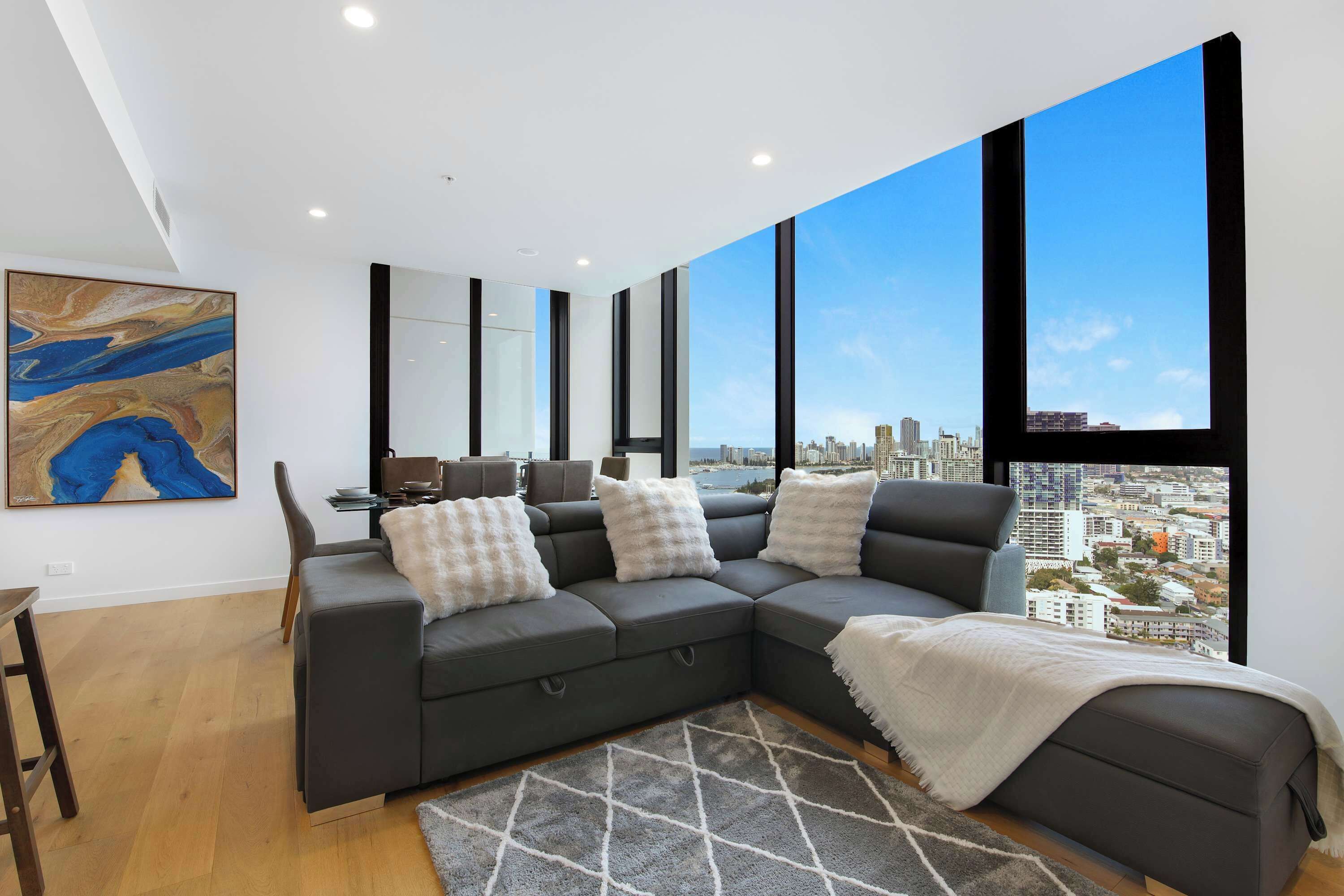 A modern living room with a sectional sofa, a dining table, and a large window offering a city view.
