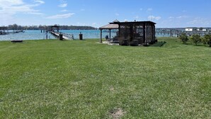 A grassy area with a gazebo, a dock, and a body of water.