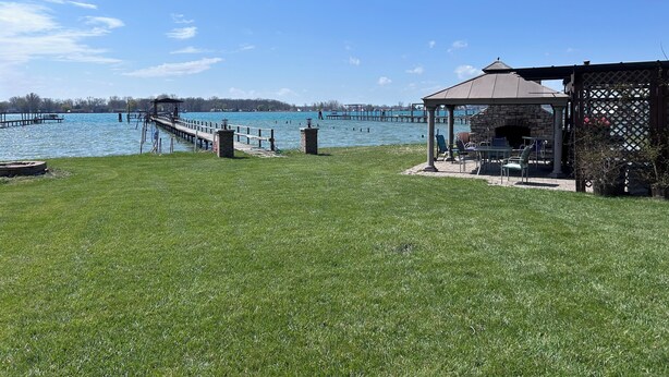 A gazebo with a stone base and a metal roof, overlooking a lake with docks and a wooden pier.