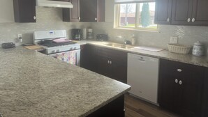 A kitchen with dark cabinets, a granite countertop, a stove, a dishwasher, and a window with blinds.