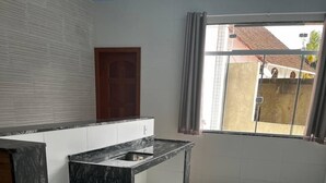 A modern kitchen with a marble countertop, wooden cabinetry, and a large window with curtains. - Hotel Lumiar (Nova Friburgo)