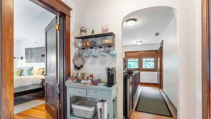 A compact kitchen with a built-in coffee machine, a small countertop, and a hanging pot rack. - Boscobel Bungalow - Walkable to Shelby Park (Nashville)