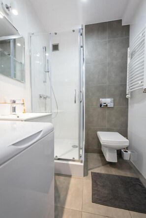 A modern bathroom with a glass-enclosed shower, a white toilet, and a vanity with a mirror. - Apartamenty 1 maja 94 (Katowice)