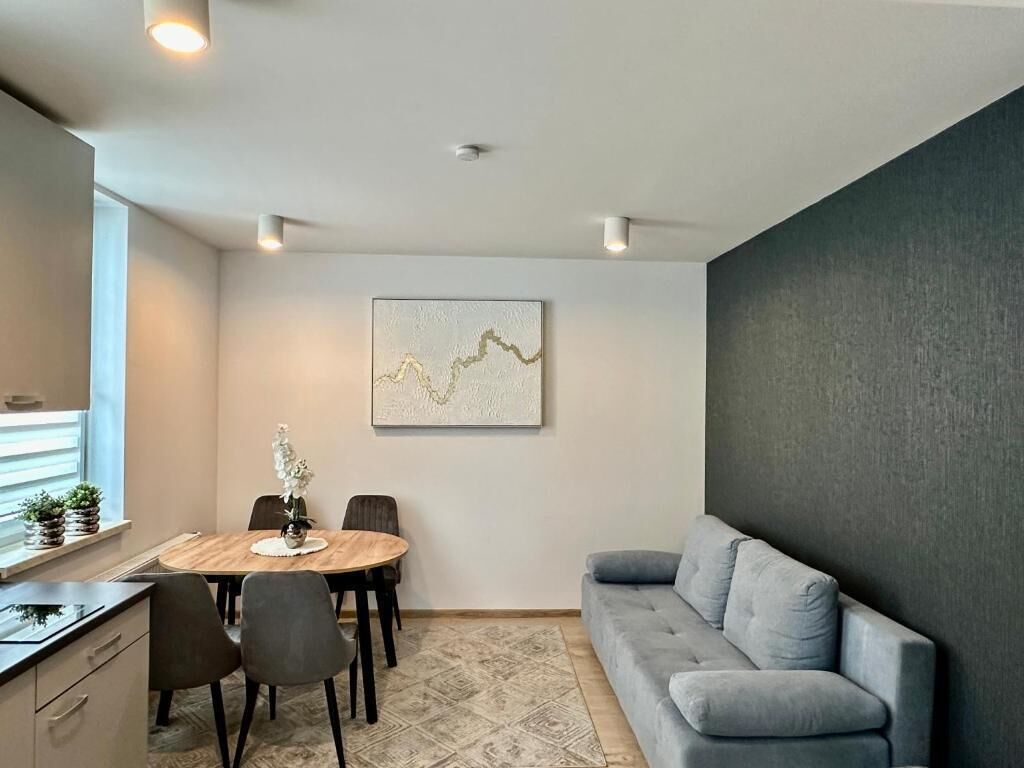 A modern living room with a gray sofa, a dining table with chairs, and a wall-mounted abstract art piece.