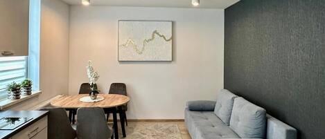 A modern living room with a gray sofa, a dining table with chairs, and a wall-mounted abstract art piece.