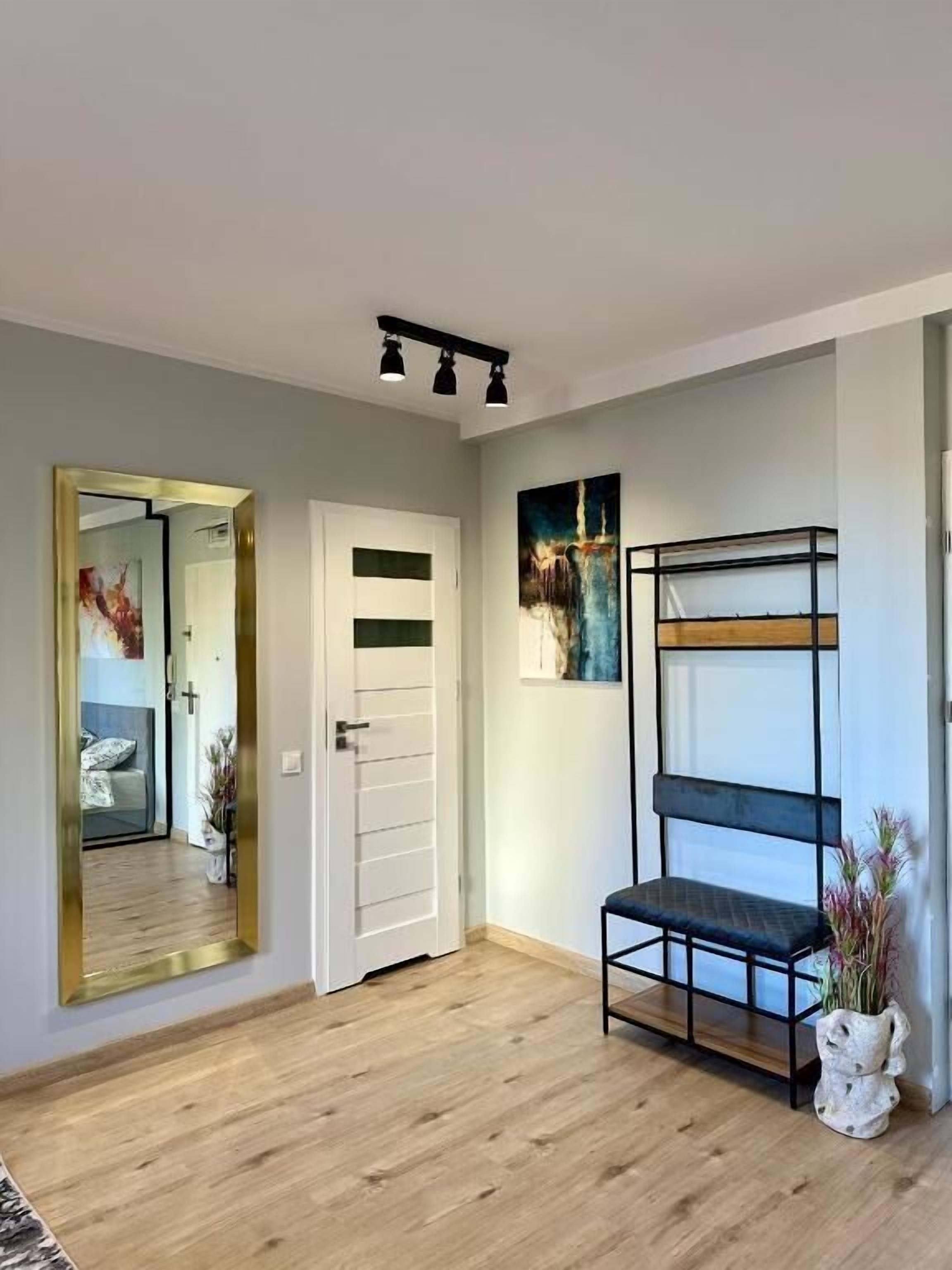 Una habitación moderna con suelo de madera, una puerta blanca, un estante de metal negro y un cuadro en la pared.