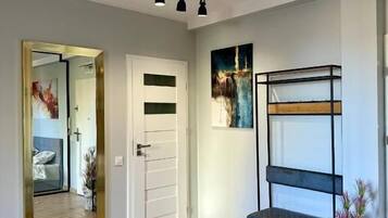 Una habitación moderna con suelo de madera, una puerta blanca, un estante de metal negro y un cuadro en la pared.