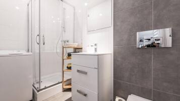 Een moderne badkamer met een glazen douchecabine, een witte wastafel met spiegel en een grijze betegelde muur.
