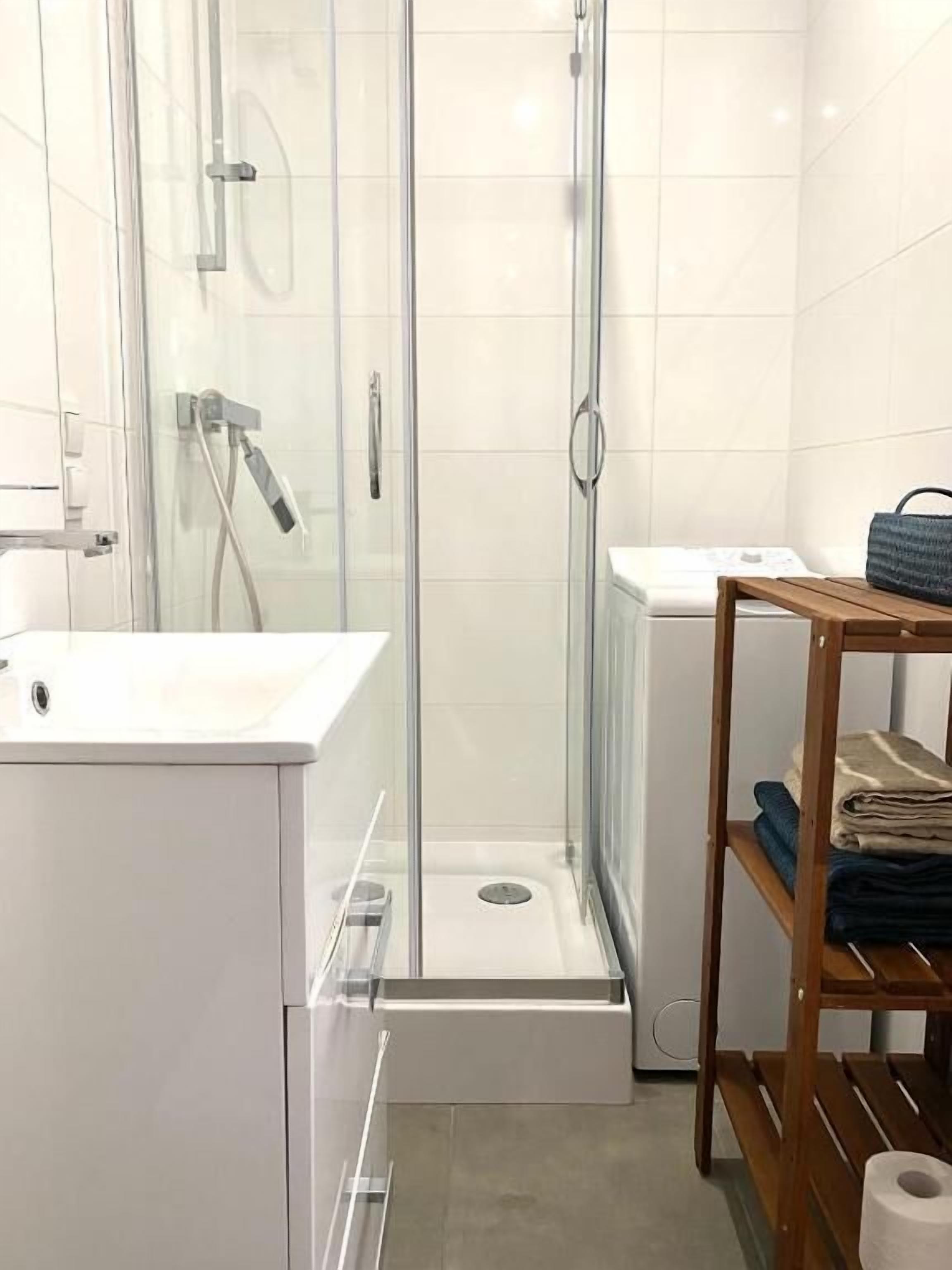A modern bathroom with a glass-enclosed shower, a white sink, and a wooden shelf with towels.