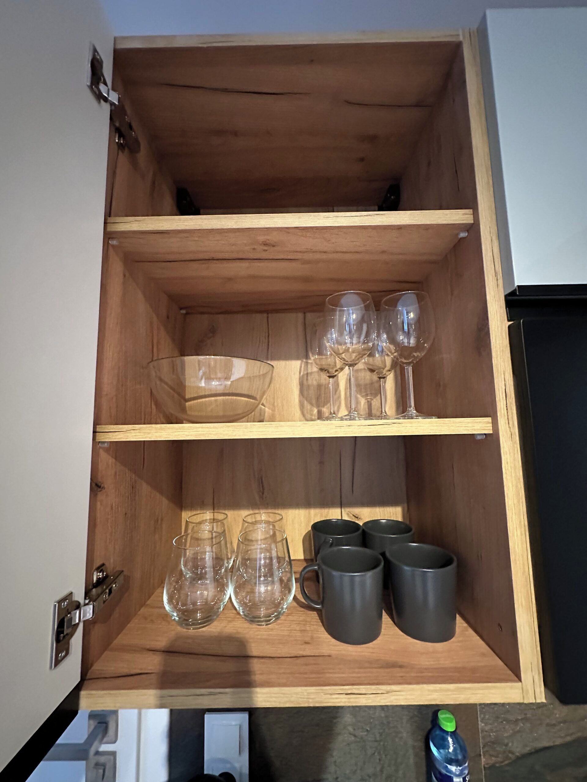 A wooden cabinet with shelves containing wine glasses and mugs.
