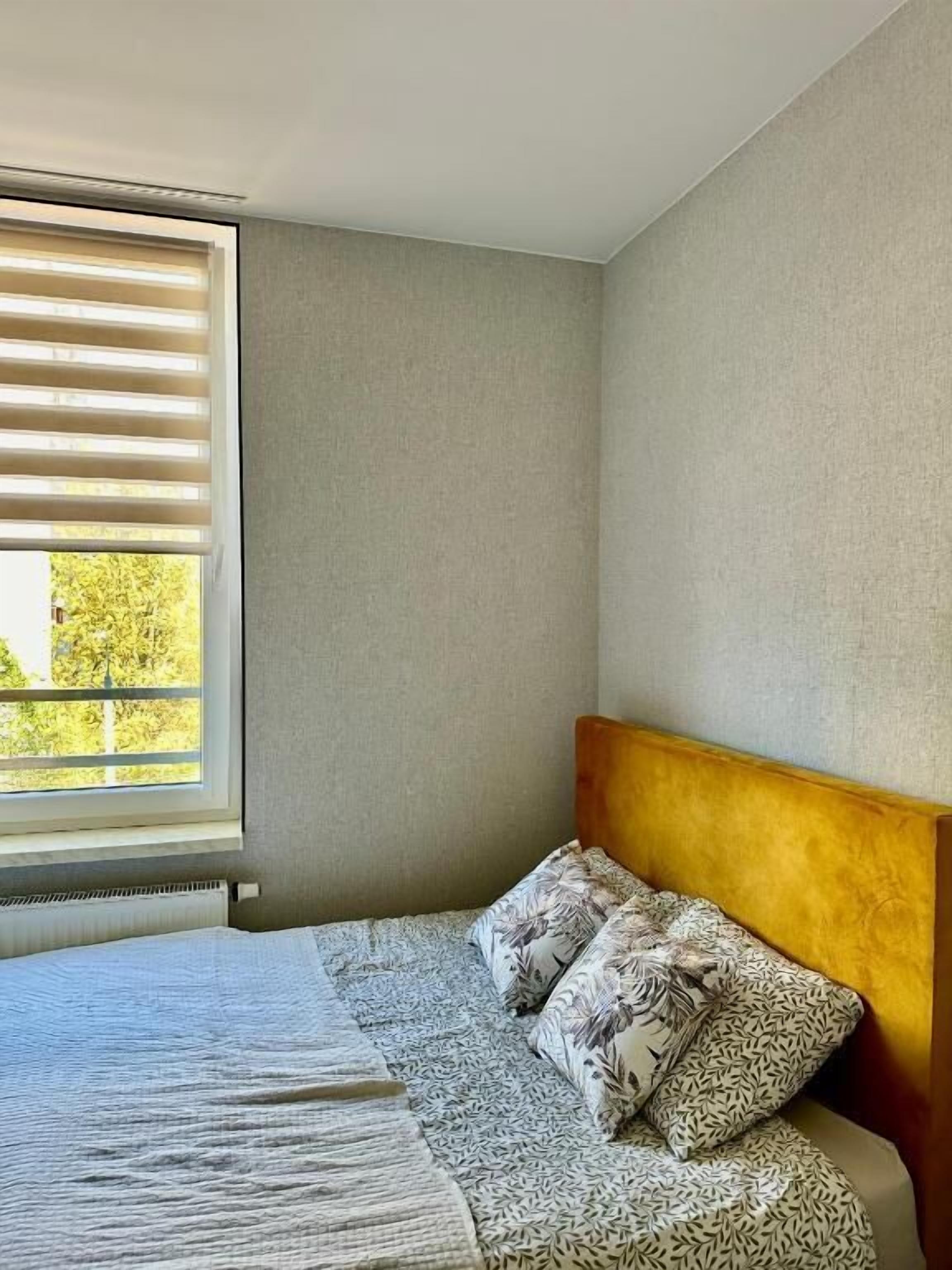 Une chambre à coucher avec un lit, une fenêtre avec des stores et un radiateur.
