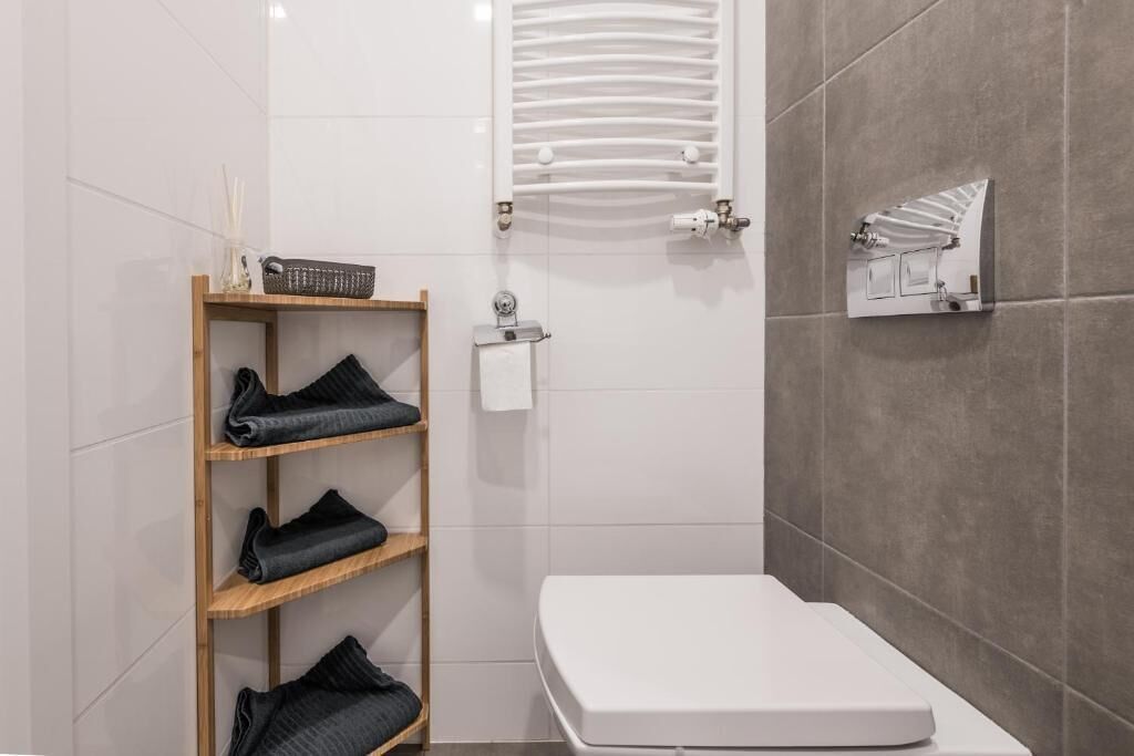 Un bagno con un WC bianco, un porta asciugamani, uno scaffale con asciugamani piegati e un termosifone.